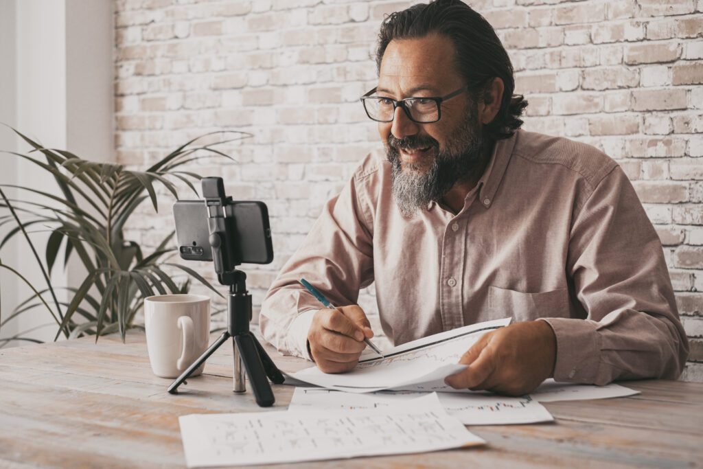 Cheerful adult man working at home office using mobile phone to film contents for the web